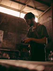 Young adult man working on a blacksmith shop showing great concentration on his job